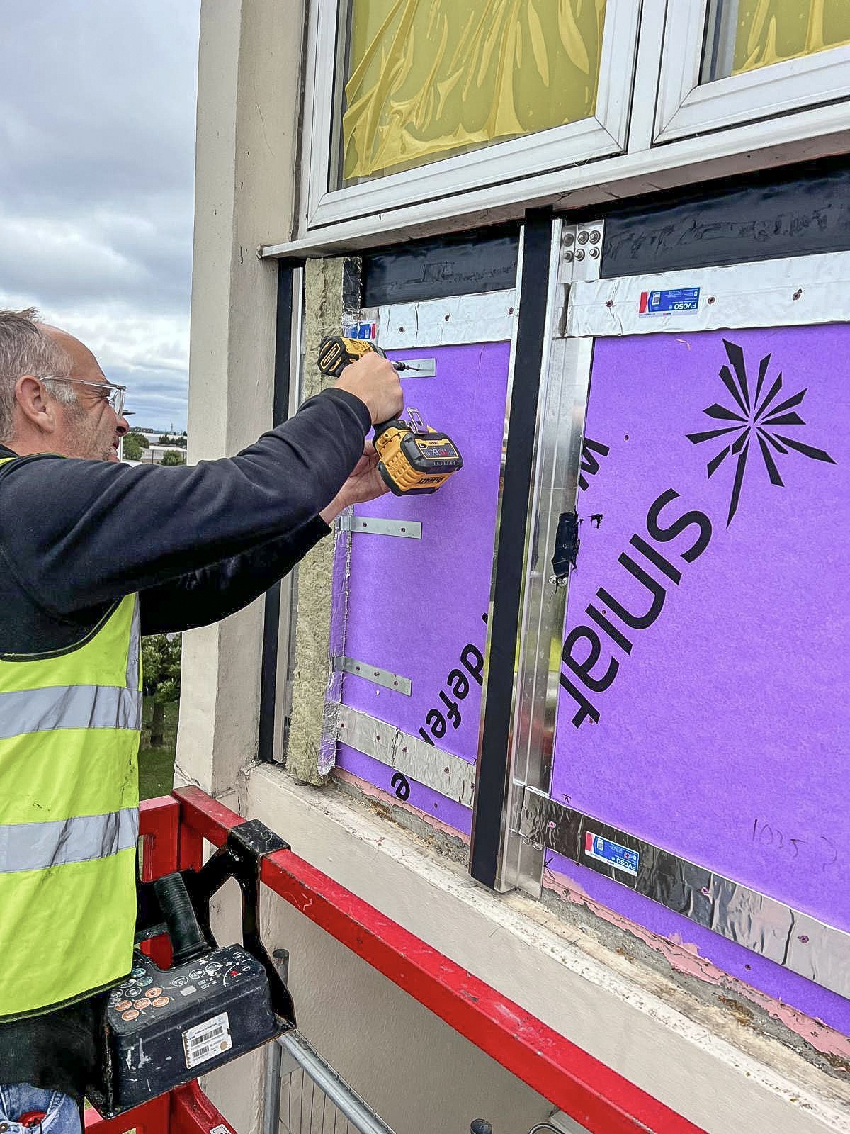 UDM operative installing purple insulation board to an existing building facade
