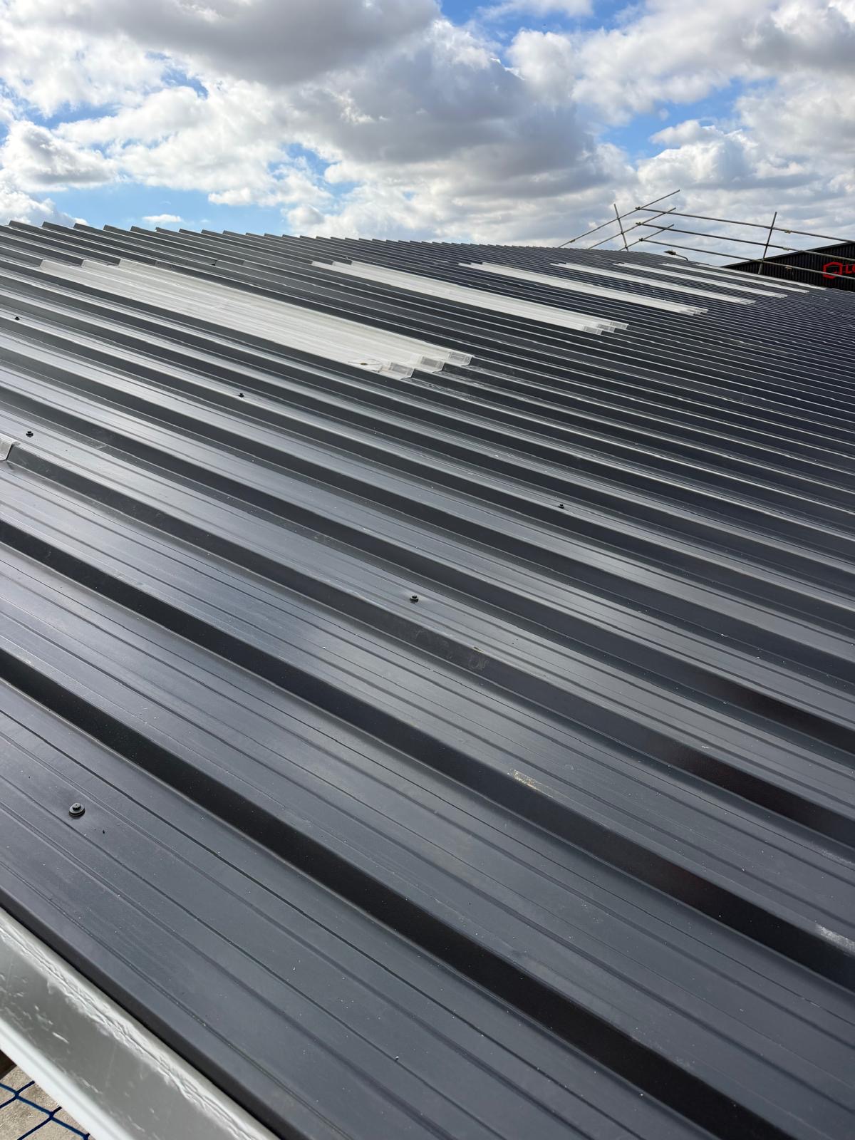 Completed industrial roof with new grey sheets and strips of rooflights