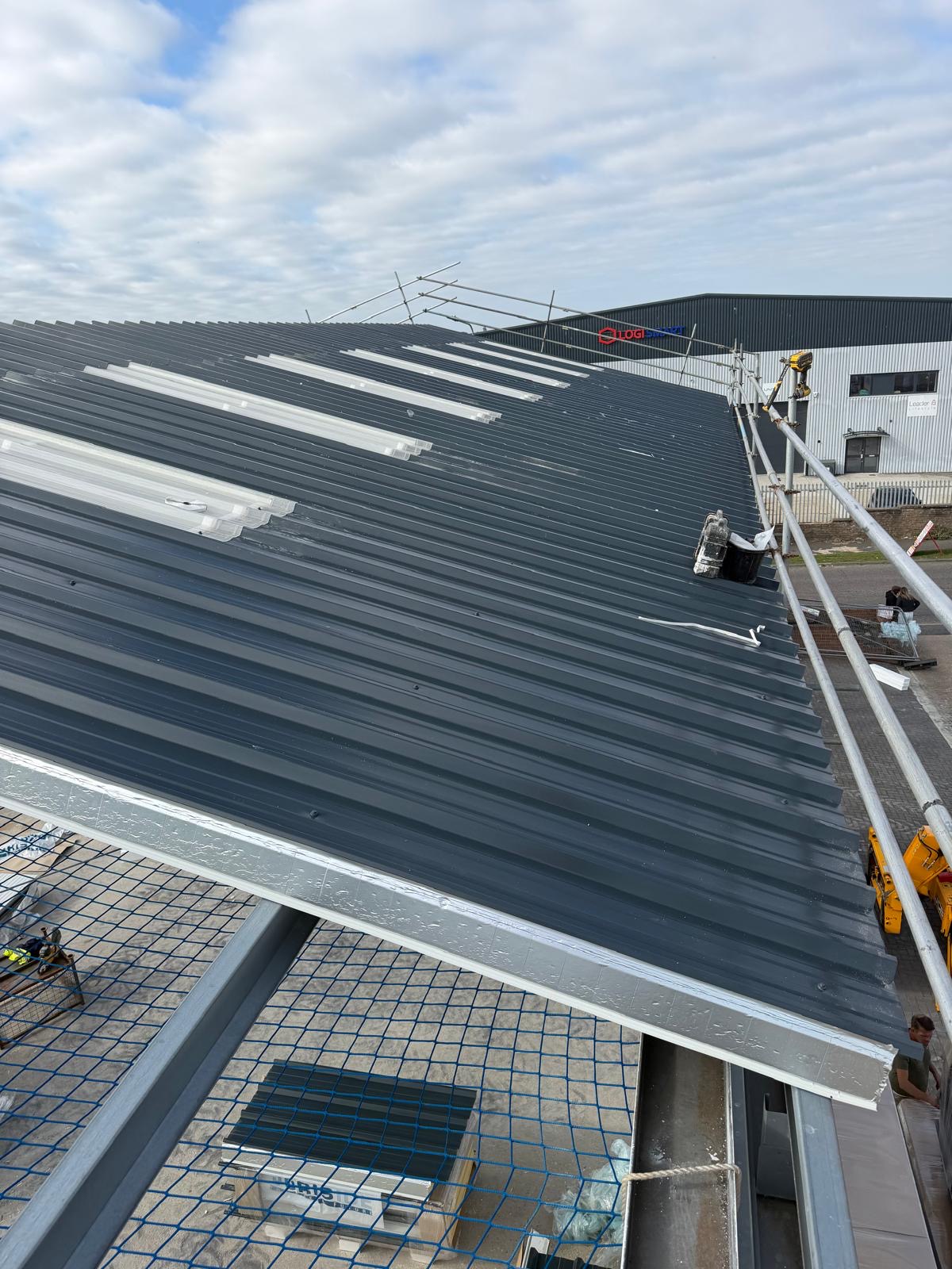 Industrial roof sheet renewal in progress beside a distribution warehouse